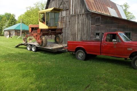 1987 Ford F-250 - Red 1987 Ford F-250 pickup truck hauls a farm implement on a trailer past a rustic barn.