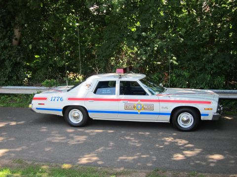 1991 Ford LTD Crown Victoria - Profile view of a white State Police sedan with red and blue stripes, 1776 markings, and a rooftop beacon.
