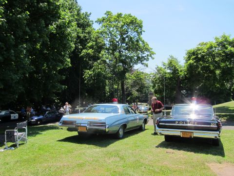 1991 Ford LTD Crown Victoria - Two vintage police sedans parked on a sunny lawn, a light blue car beside a black Police-marked car.