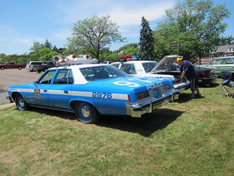 1991 Ford LTD Crown Victoria - blue police sedan marked 2976 with its hood raised, parked on grass among other cruisers at a show.