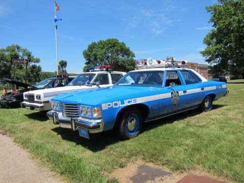 1991 Ford LTD Crown Victoria - Blue and white Police-marked sedans parked on a lawn near a flagpole flying the American flag.