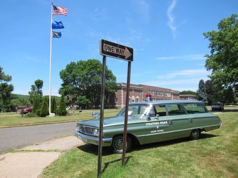 1991 Ford LTD Crown Victoria - green Stratford Police radio-patrol station wagon parked behind a One Way sign, with an American flag flying.