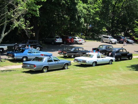 1991 Ford LTD Crown Victoria - row of classic police patrol cars, including light-blue and silver sedans, displayed on a grassy field at a car show.