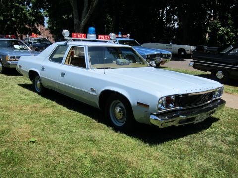 1991 Ford LTD Crown Victoria - white Plymouth police sedan with a State Police light bar parked on a grassy field among other cruisers.