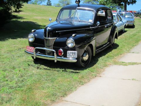 1991 Ford LTD Crown Victoria - black late-1940s Ford sedan bearing a red State Police front plate parked on a grassy field at a show.