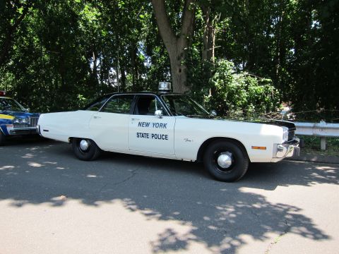 1991 Ford LTD Crown Victoria - white Plymouth sedan lettered New York State Police parked on a tree-lined paved road.