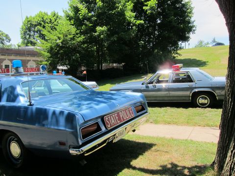 1991 Ford LTD Crown Victoria - Rear three-quarter view of a blue State Police sedan with red plate, a second cruiser parked alongside on grass.