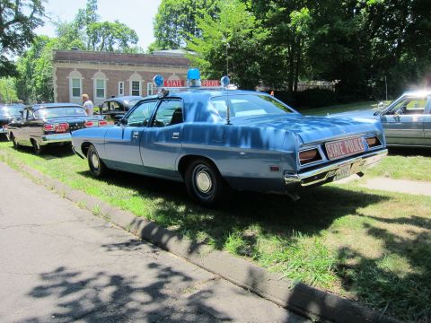 1991 Ford LTD Crown Victoria - Rear view of a light-blue State Police sedan with roof lights parked on grass before a brick building.