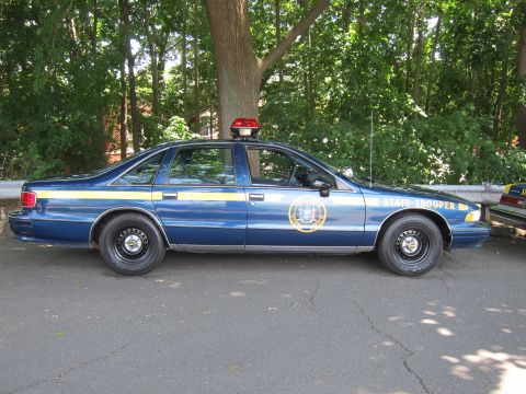 1991 Ford LTD Crown Victoria - dark-blue Chevrolet Caprice marked State Trooper with a gold door seal shown in side profile on a paved road.