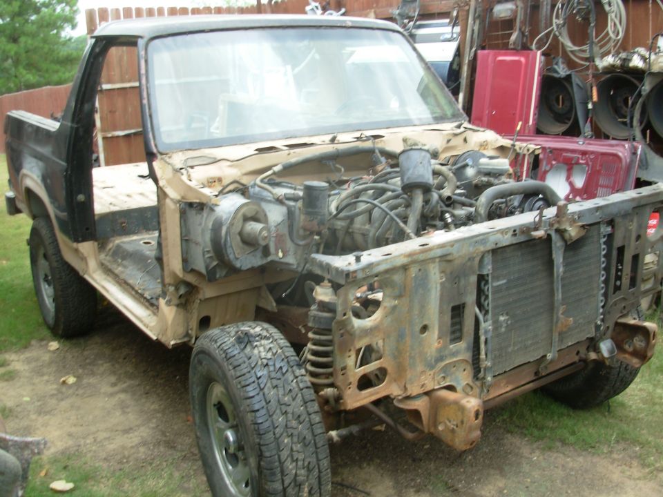 Heavily stripped pickup truck with exposed engine bay and rust damage in backyard