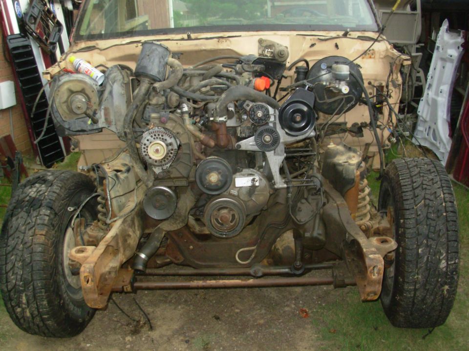 Front of tan Ford truck with grille removed exposing engine and pulleys