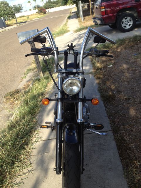 1995 Ford Bronco - A motorcycle with custom tall handlebars is parked on a sidewalk next to a street.