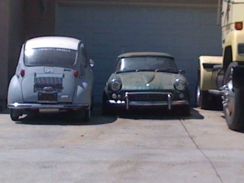 1968 Ford Mustang - Two classic cars, a Subaru 360 and a Triumph Spitfire, are parked in front of a garage door.