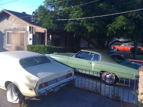 1968 Ford Mustang - A yellow 1971-1973 Ford Mustang is parked next to a green car in front of a house.