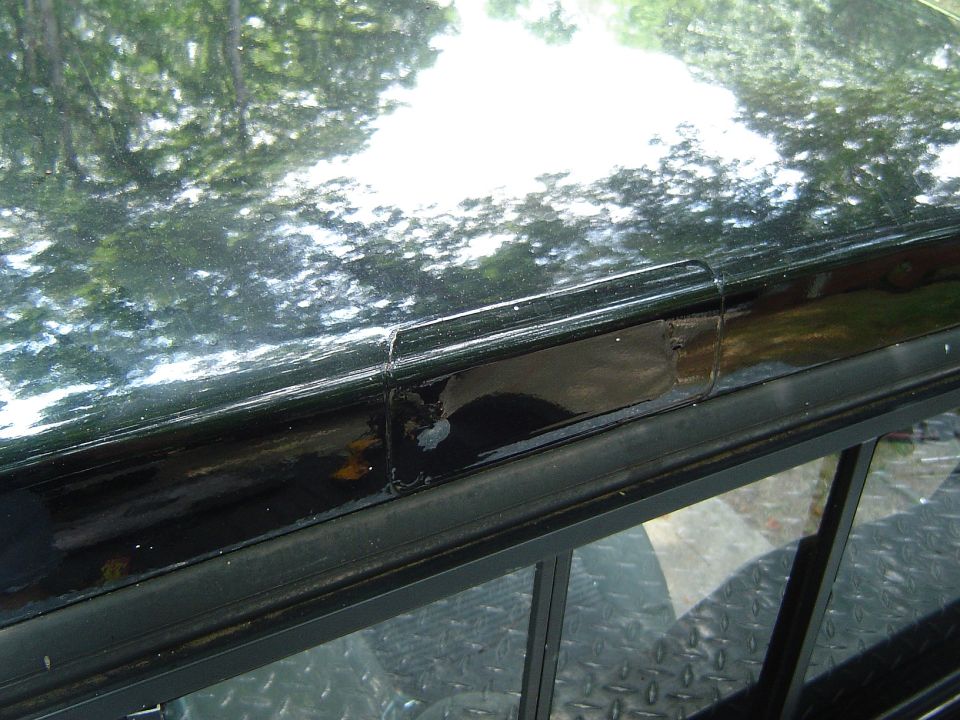 Black truck bed rail with peeling paint and a small dent