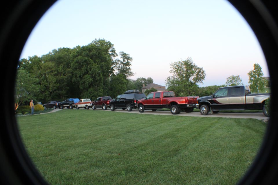 Line of trucks and SUVs parked along a driveway at dusk, shot through a round lens vignette
