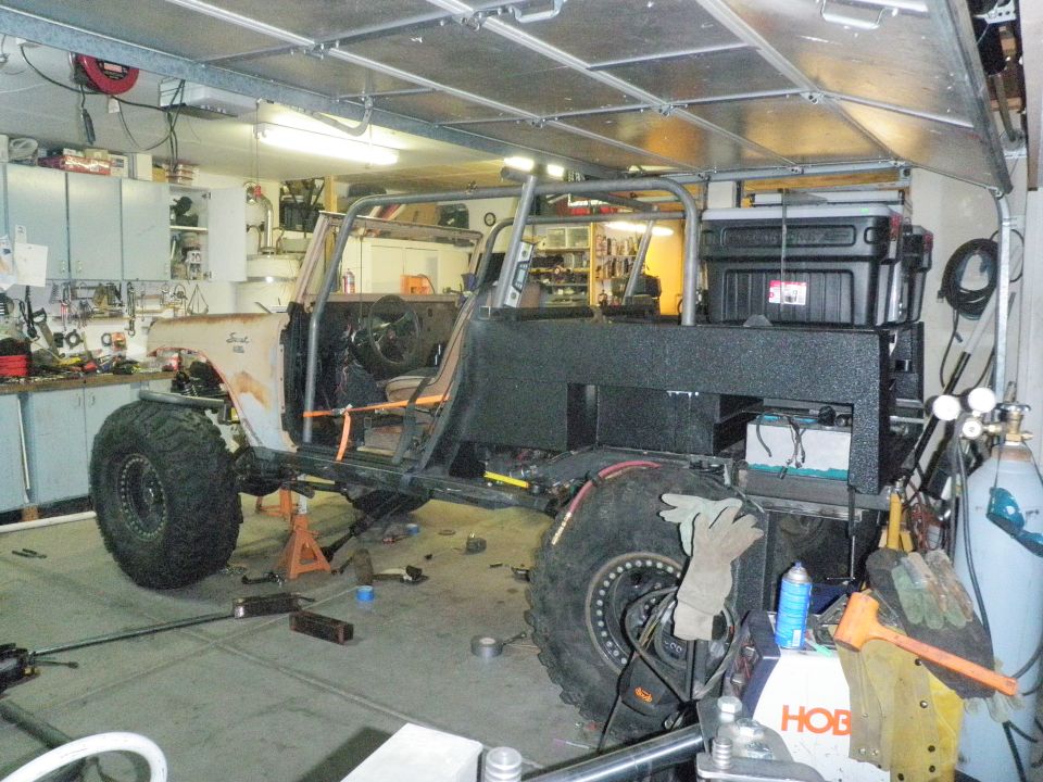 1961 International Scout 800 with custom roll cage and large tires, seen from the side in a garage