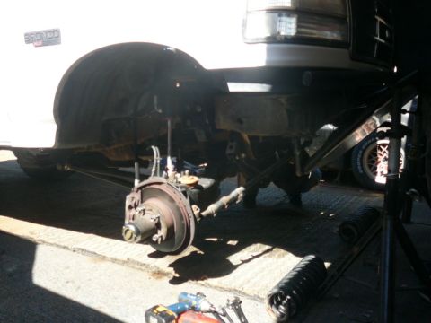 1988 Ford Bronco - Front suspension of a white Ford Bronco undergoing maintenance, with a visible fender badge.