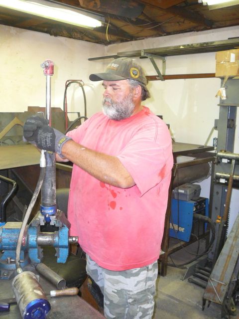 1988 Ford Bronco - A man is working on a part clamped in a vise in a garage setting, with tools and equipment visible.