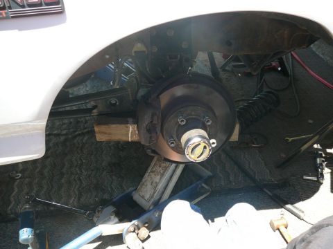 1988 Ford Bronco - Close-up of a vehicle's front wheel hub and brake assembly, supported by a jack and wooden blocks.