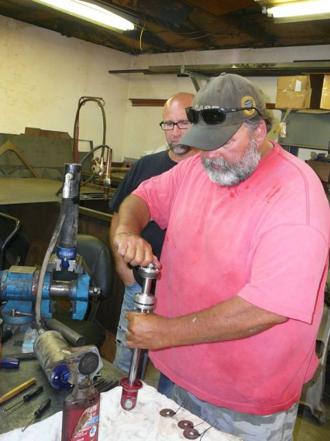1988 Ford Bronco - Mechanic works on a shock absorber assembly in a garage setting, with another person observing.
