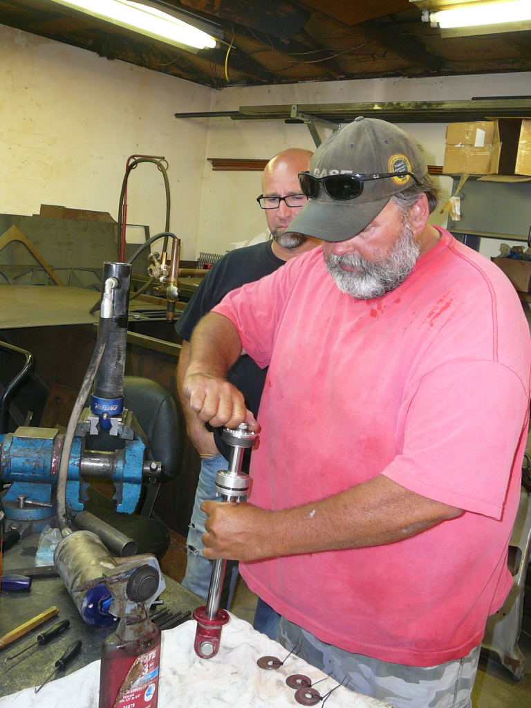 Man assembling a red and silver shock absorber in a vise