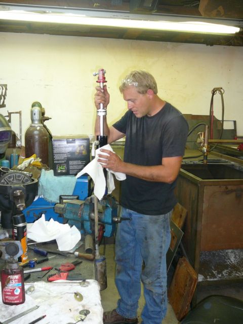 1988 Ford Bronco - Man cleans a car part in a workshop setting with tools and equipment around.