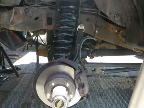 1988 Ford Bronco - Close-up of the front suspension and brake system of a 1988 Ford Bronco, showing mechanical components and some rust.