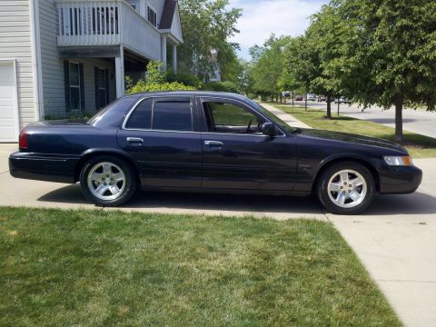 1999 Mercury Grand Marquis - Dark blue Mercury Grand Marquis sedan sitting on a residential driveway, shown in near-full passenger-side profile with tinted glass and a…