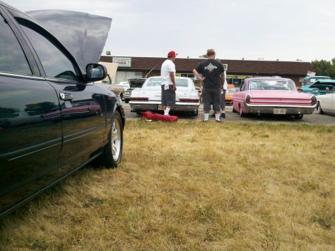 1999 Mercury Grand Marquis - A dark sedan is parked with its hood open at an outdoor car show, alongside several other classic vehicles.