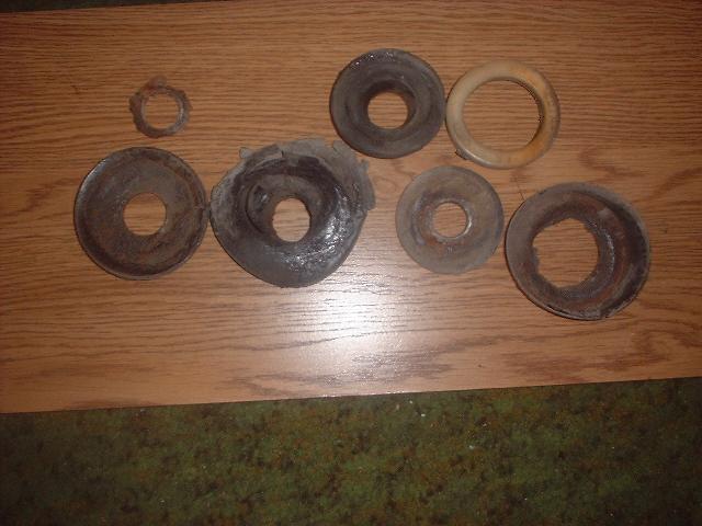 Seven worn rubber and metal coil spring isolators and one tan poly ring laid out on a wood table