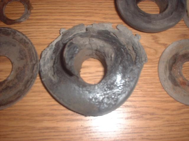 Worn, cracked rubber coil spring isolators from a Ford Bronco laid on a wooden table