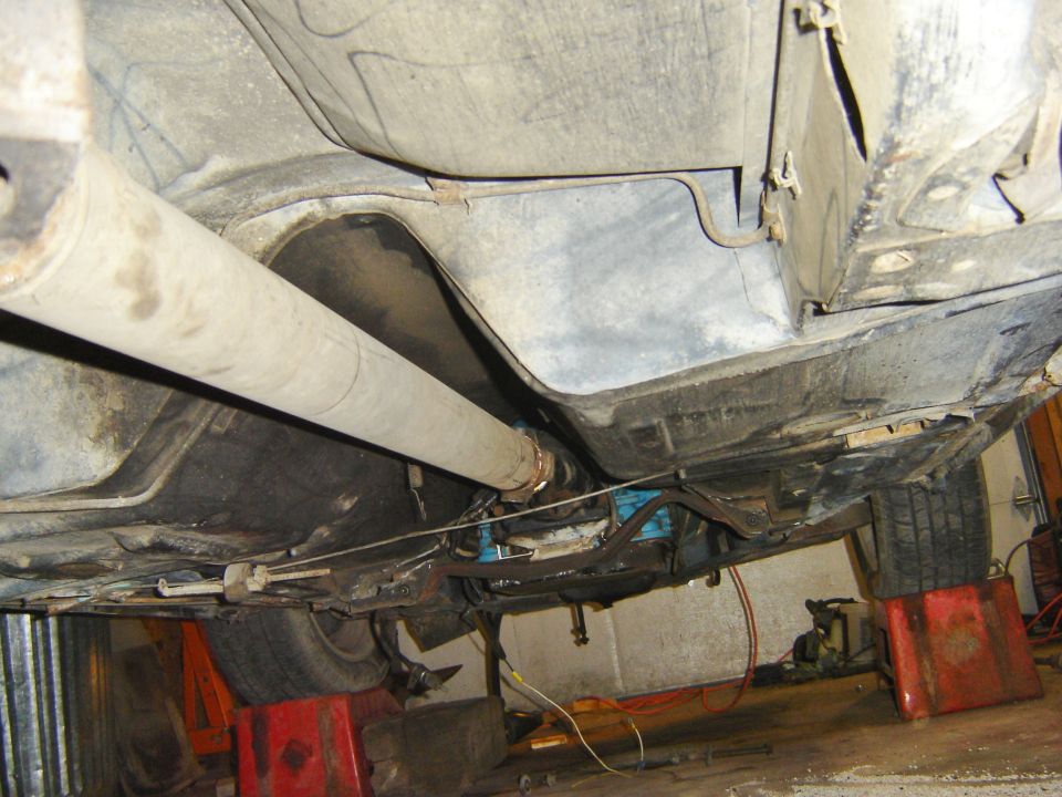 Underside of a vehicle on jack stands, showing the drive shaft and exhaust system