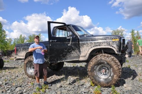 1986 Ford F-150 - A heavily modified 1986 Ford F-150 pickup truck sits off-road, its driver's side door ajar.