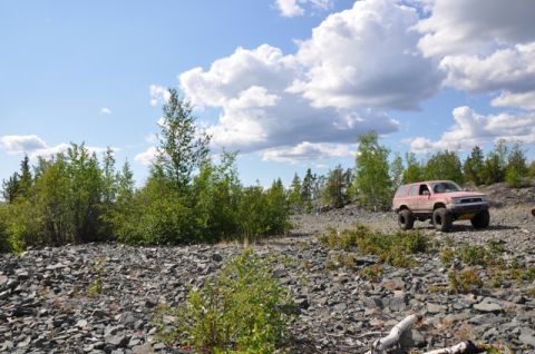 1986 Ford F-150 - Red SUV navigates a rough, rocky landscape on a sunny day with scattered clouds.