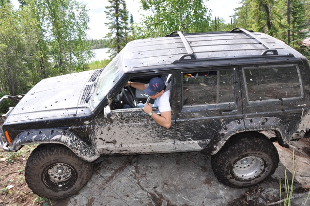Mud-covered Jeep Cherokee XJ navigating rocks with a driver inside
