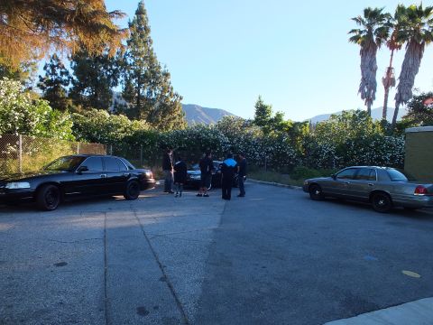2003 Ford Crown Victoria - Black and silver Crown Victoria sedans in a parking lot, people gathered near them with hills in the distance.