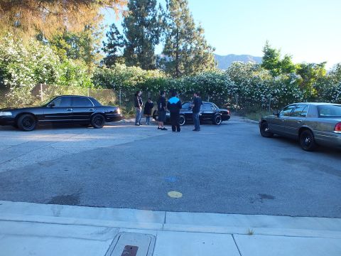 2003 Ford Crown Victoria - Several people stand among black and silver Crown Victoria sedans parked in a sunny lot near hills.