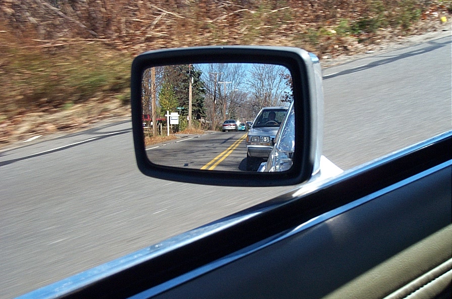 Side mirror view of cars on a road with yellow lines