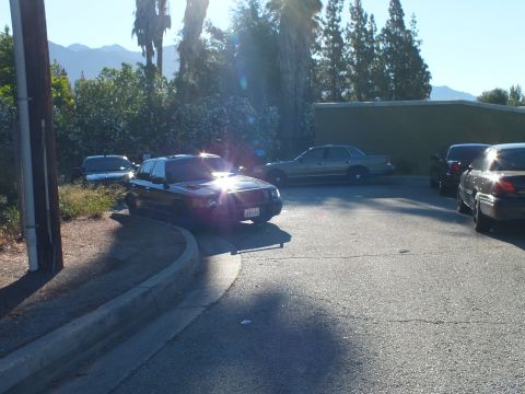 2003 Ford Crown Victoria - black Ford sedan catches sun glare at a lot curve with a silver sedan parked behind.