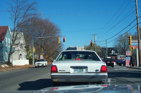 1991 Ford LTD Crown Victoria - A white 1991 Ford Crown Victoria LTD is seen from behind while driving on a street with other vehicles and buildings.