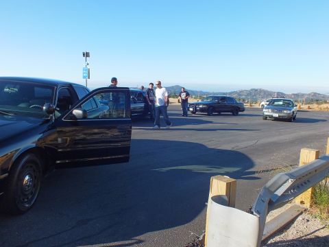 2003 Ford Crown Victoria - Open-door black full-size sedan at a roadside meet with guardrail and distant hills