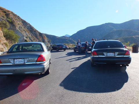 2003 Ford Crown Victoria - Two Panther sedans parked tail-out with people and canyon ridges in the distance