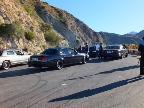 2003 Ford Crown Victoria - Black full-size sedans on staggered wheels lined up beside a steep rock cutaway