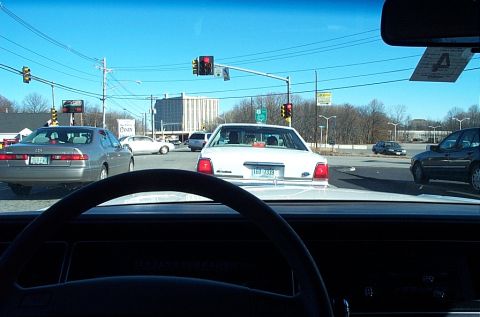 1991 Ford LTD Crown Victoria - A white sedan is stopped at a traffic light, with other cars around it.