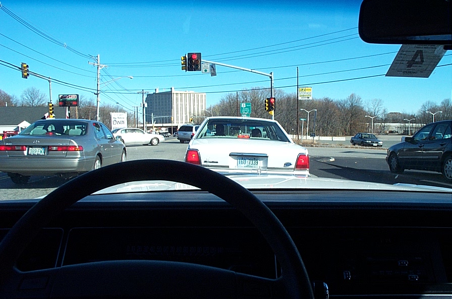 White sedan with a license plate reading TGU 7339, seen from behind at an intersection