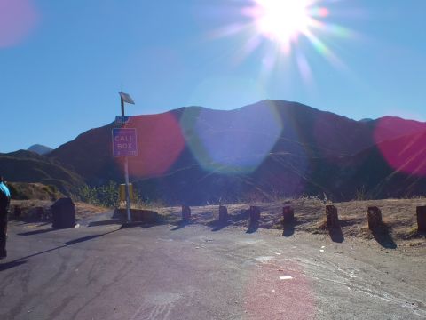 2003 Ford Crown Victoria - Roadside emergency call-box sign and wooden posts below a backlit mountain ridge