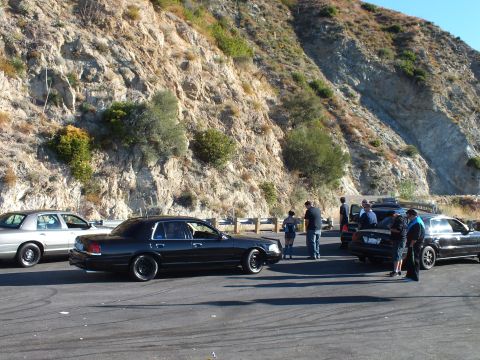 2003 Ford Crown Victoria - Cluster of lowered black sedans and bystanders against a steep tan hillside