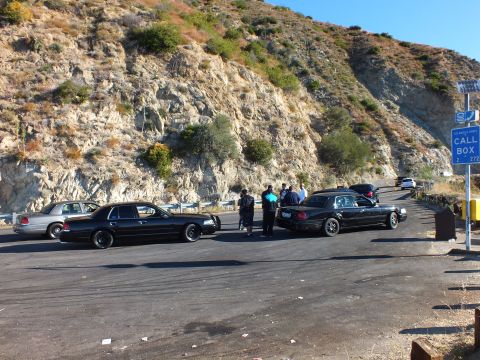 2003 Ford Crown Victoria - Black full-size sedans and a silver one gathered beside a rocky slope and call box