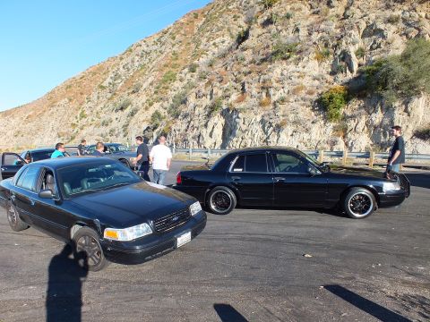 2003 Ford Crown Victoria - Pair of black Ford full-size sedans facing forward at a rocky canyon meet
